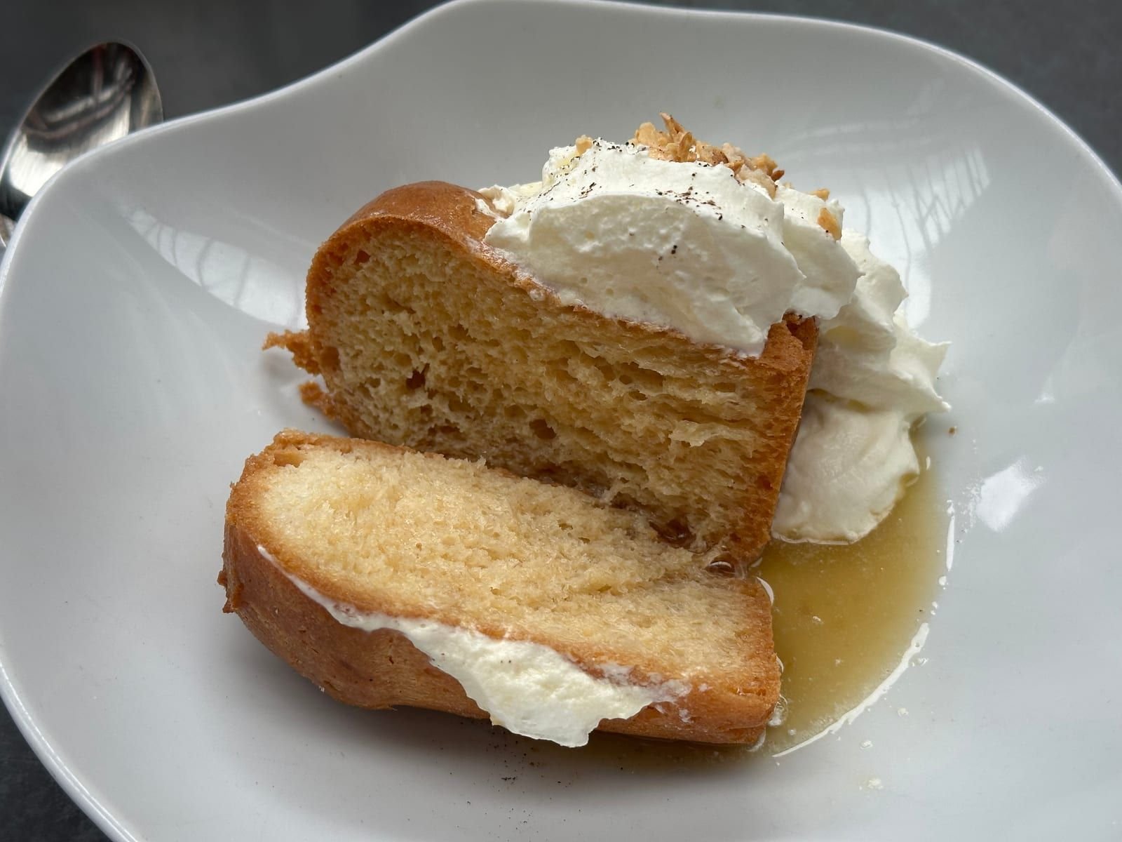 Un baba au rhum imbibé, servi avec de la crème fouettée dans une assiette creuse.
