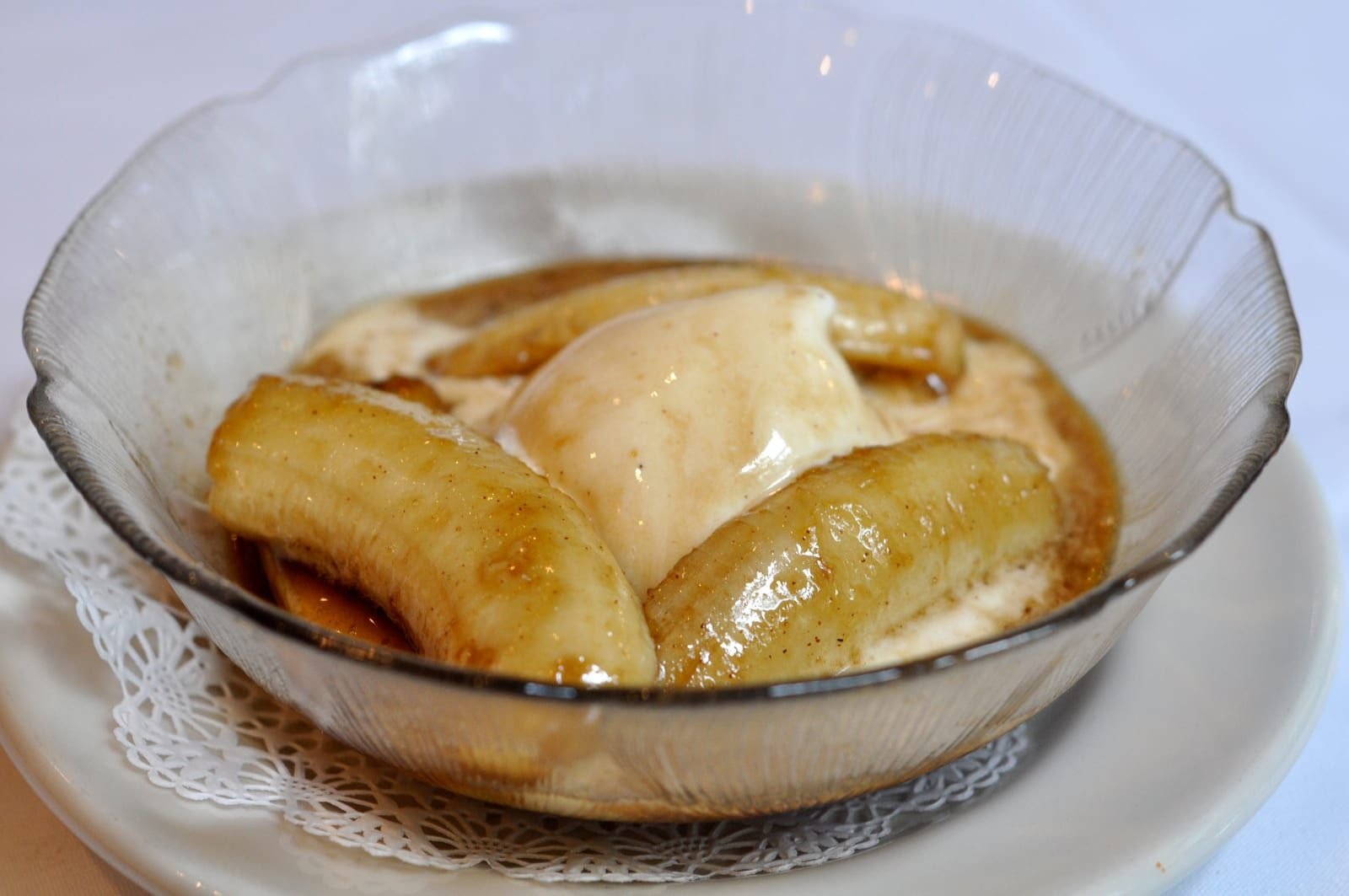 Des demi-bananes caramélisées nappées de sauce brune, servies avec une boule de glace vanille dans une coupe en verre.
