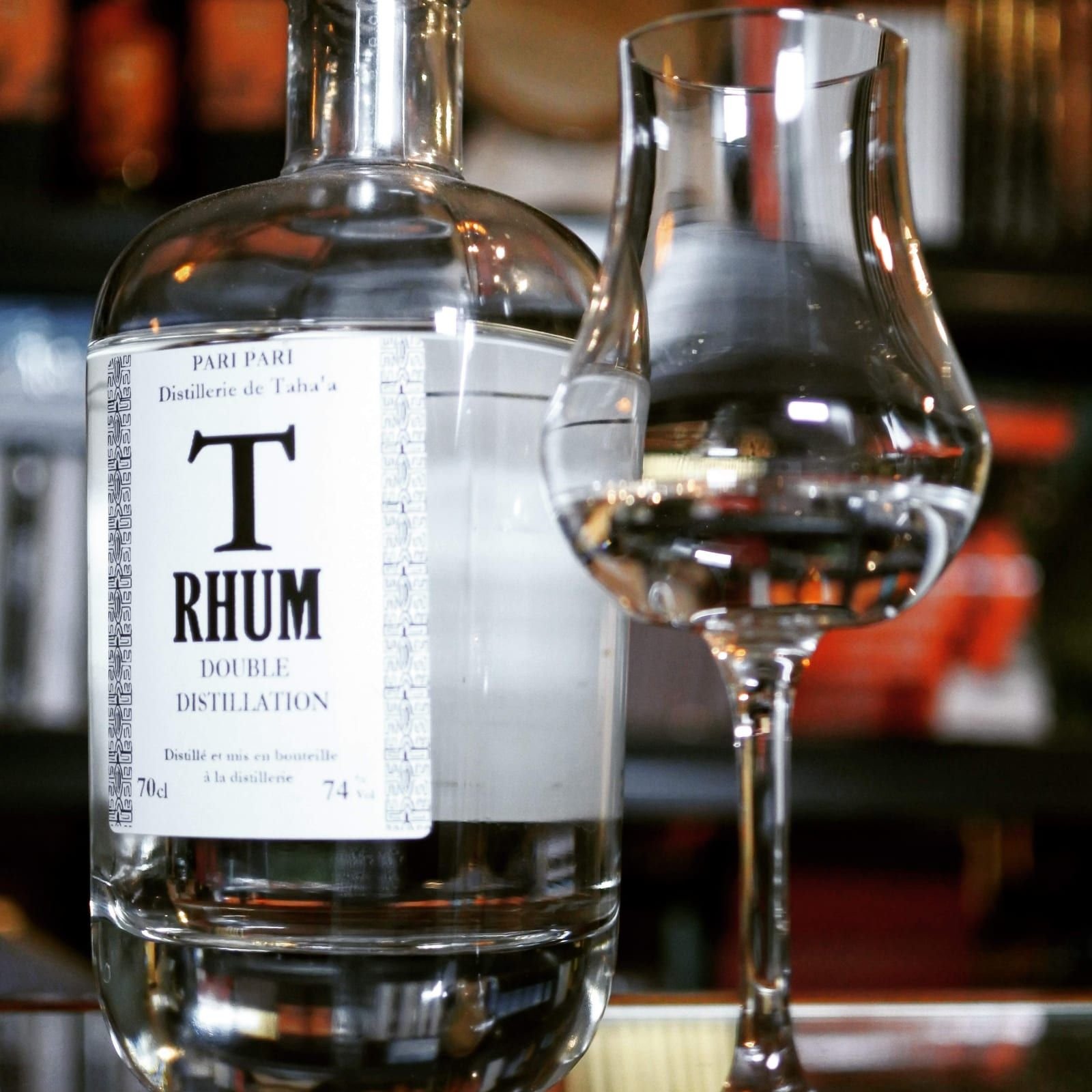 Une bouteille de rhum blanc Pari Pari T Rhum posée à côté d'un verre tulipe contenant une petite dose de rhum, sur un comptoir.